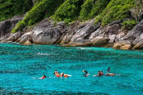 Tourists swimming in crystal-clear blue waters of the Aman Islands, surrounded by a stunning tropical landscape.