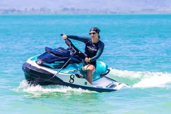 Woman confidently riding a jet ski on vibrant blue ocean waves in Phuket under a clear sky.