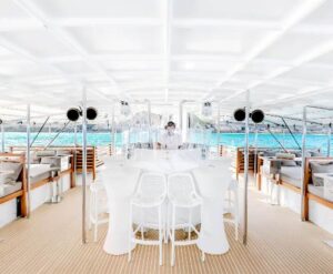 A boat's bar area featuring white chairs and tables, elegantly arranged for a relaxing atmosphere on the water.