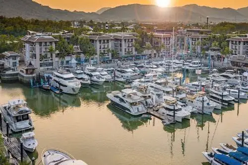 The sun sets below the horizon, casting a peaceful glow over a marina filled with boats, enhancing the natural beauty of the scene. Ideal for Phuket Boat Tour to James Bond Island.