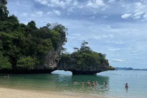 A group of people swimming in the ocean, with a striking rock formation visible in the background.