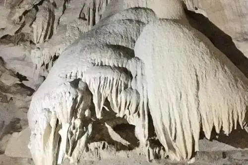 Inside a cave, large white formations rise dramatically, creating a captivating and serene underground environment.