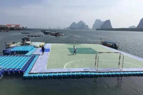 A vibrant soccer field floating on water at Koh Panyee, with players in an energetic match under a clear sky.