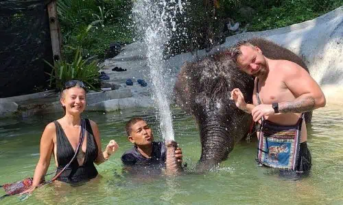 Eine Familie erlebt einen fröhlichen Moment im Wasser mit einem Elefanten und betont die Schönheit der Natur sowie die Verbindung zwischen Mensch und Tier.