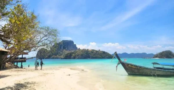 Ein Boot ruht am Sandstrand neben einer kleinen Hütte, umgeben von einer ruhigen Küstenlandschaft.