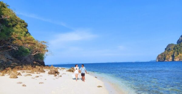 Two individuals stroll along the sandy beach, with the ocean waves gently lapping at the shore beside them.