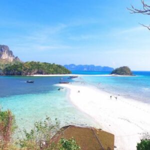 A serene view of Krabi's beach in Thailand, featuring soft sands and gentle waves under a clear blue sky.