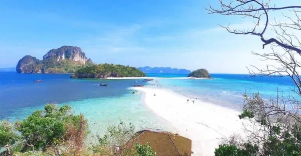 A serene view of Krabi's beach in Thailand, featuring soft sands and gentle waves under a clear blue sky.