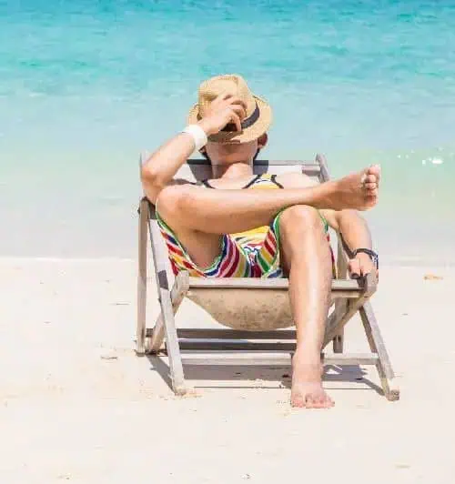 A man wearing a hat and striped shorts sits in a beach chair, enjoying the sun and ocean view.