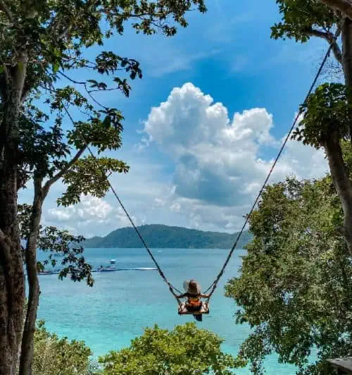 A person swings gently, gazing at the vast ocean horizon under a clear blue sky.