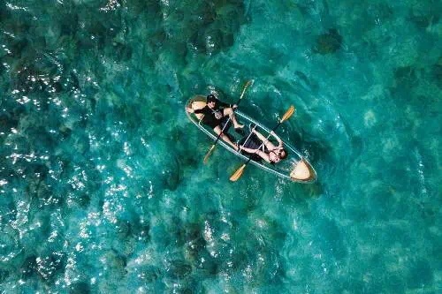 Two individuals paddling a canoe on calm ocean waters near Coral Island, enjoying the tropical serenity under a bright blue sky.