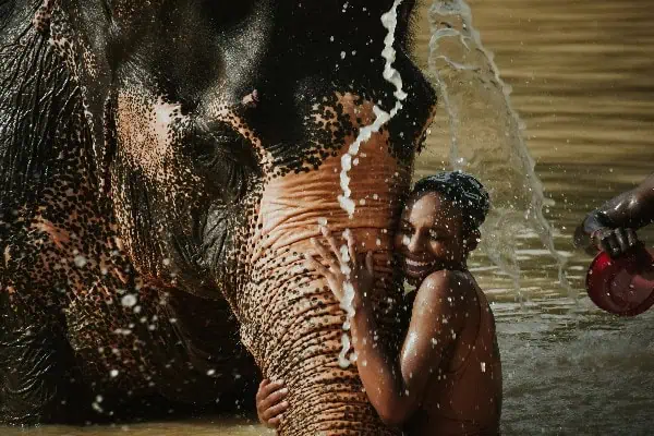 A woman washes an elephant in a body of water, creating splashes as they enjoy a refreshing bath together.