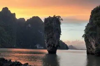 The sun dips below the horizon, illuminating the water and rocks with a golden glow during sunset at James Bond Island.