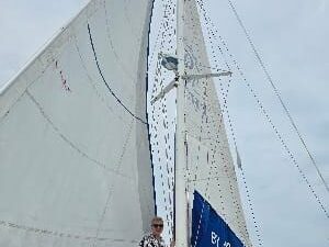 Young man in front of the white sails of a catamaran, with the vast sea and clear sky in the background.
