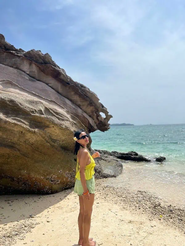 Woman in a yellow top standing on the white sandy shore of Khai Island, with the ocean and blue sky behind her.