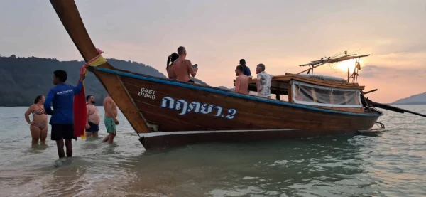 Personen am Strand neben einem Boot, genießen das schöne Wetter und die Aussicht auf das Meer.