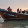 People on the beach next to a boat, enjoying the beautiful weather and the view of the sea.