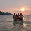 People stand in the water at sunset, golden rays illuminate the peaceful landscape.