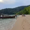 Boat on a sandy beach, surrounded by tropical forest and lush greenery.