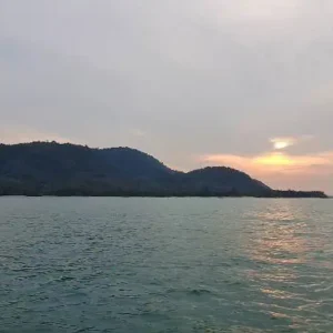 Thailändisches Boot auf stillem Meer bei Sonnenuntergang, Berge im Hintergrund in goldenem Licht.