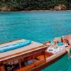 A person sits in a longtail boat floating on calm water, surrounded by a serene natural landscape.