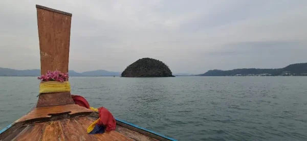 Traditionelles Longtail-Boot auf türkisfarbenem Wasser vor einer grünen Insel bei einer privaten Bootstour in Phuket.