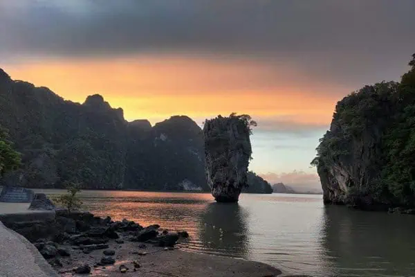 The sun dips below the horizon, illuminating the water and rocks with a golden glow during sunset at James Bond Island.