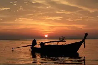 A Longtailboot gently floating on the water during a serene sunset, with warm hues illuminating the peaceful scene.