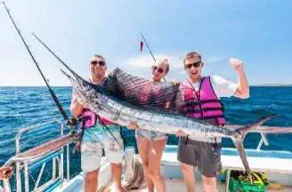 Three individuals proudly holding a sailfish on a boat, celebrating their successful catch during a thrilling deep-sea fishing adventure in Phuket.