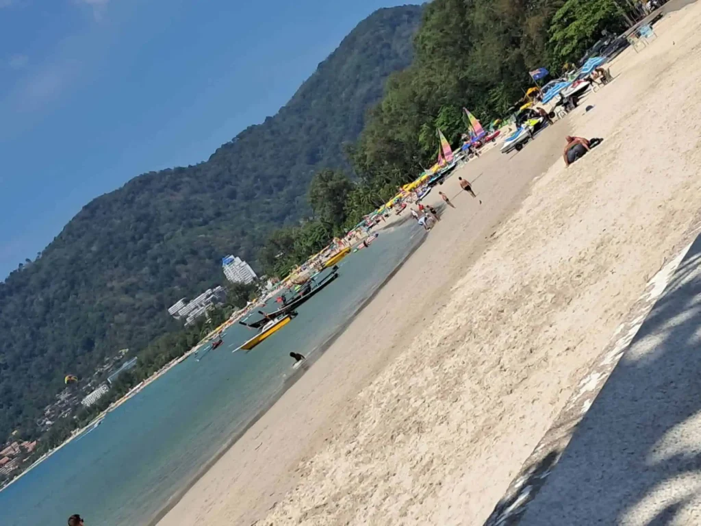 A vibrant scene at Patong Beach, Phuket, with beach goers relaxing and boats sailing in the turquoise water.
