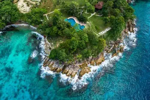 Aerial view of a tropical island with a serene pool, surrounded by lush greenery, sandy beaches, and crystal-clear waters, perfect for a peaceful getaway.