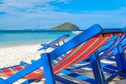 Gestreifte Strandstühle in Blau und Rot, die am Sandstrand einer tropischen Insel aufgestellt sind, ideal zum Entspannen am Meer.