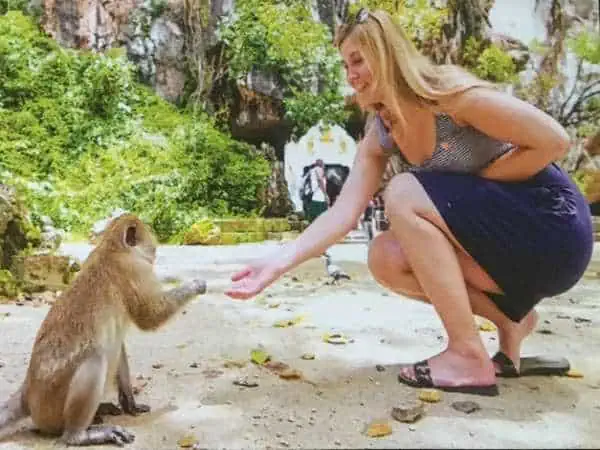 A woman gently pets a monkey sitting on the ground, showcasing a moment of connection between human and animal.