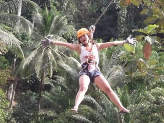 A woman ziplining gracefully through a lush green jungle, surrounded by vibrant foliage and sunlight filtering through the trees.