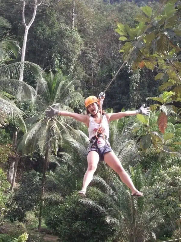 A woman ziplining gracefully through a lush green jungle, surrounded by vibrant foliage and sunlight filtering through the trees.