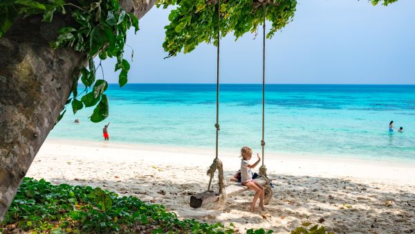 A woman enjoys a serene moment sitting on a swing, overlooking the tranquil beach and gentle waves.