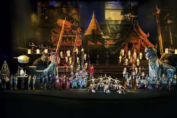 A large audience gathers in front of the grand stage for the Siam Niramit Show in Phuket, where performers showcase vibrant Thai cultural traditions through stunning music, dance, and elaborate costumes. The stage is adorned with colorful lights, and the atmosphere is filled with excitement as spectators enjoy this awe-inspiring cultural performance.