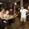 Eine Familie mit vier Personen genießt eine Mahlzeit an einem Holztisch bei der Siam Niramit Show in Phuket, umgeben von kultureller Atmosphäre.