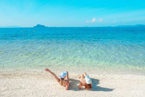 Two women relaxing on the beach, enjoying the sun and the warm sand beneath them.