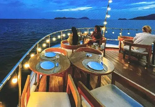 Personen genießen eine Nacht auf einem Boot, sitzen an Tischen, während das ruhige Wasser die sanften Lichter um sie herum widerspiegelt.