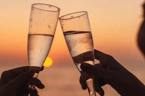 Two individuals clink champagne glasses against a vibrant sunset, celebrating a romantic moment during a sunset cruise.