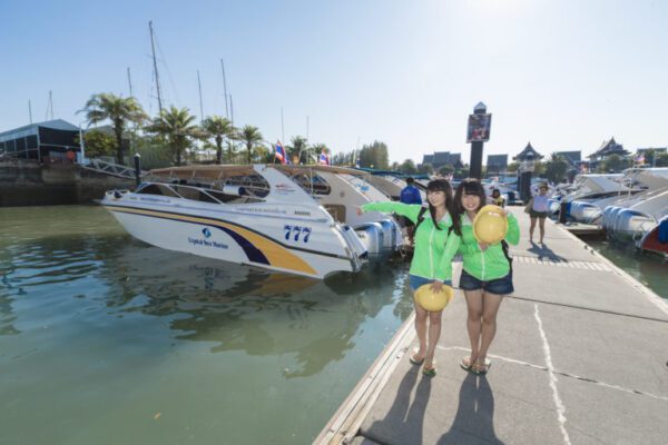 Two women in green jackets stand beside a boat, smiling and enjoying a sunny day by the water.