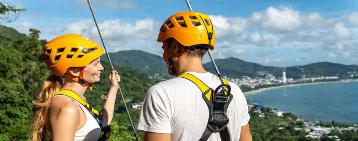 Two people enjoying a thrilling zipline ride through vibrant jungle greenery in Phuket.