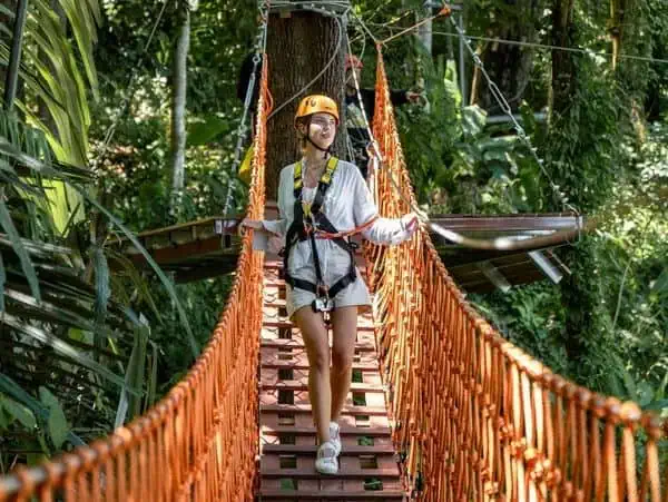 Woman walking on a bridge through a lush jungle in Phuket, surrounded by vibrant greenery and tropical foliage.