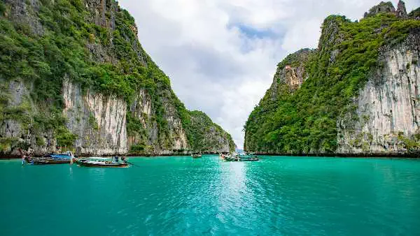 Boote schaukeln auf türkisfarbenem Wasser, umgeben von einer malerischen Bucht und grüner Küstenlandschaft.