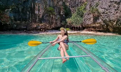 A woman paddling a boat on clear water, surrounded by a serene and scenic environment.