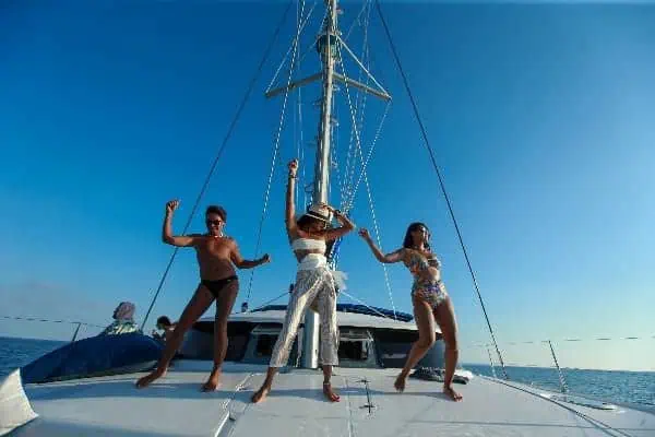Drei Frauen in Bikinis sitzen auf dem Bug eines Bootes, genießen die Sonne und den Blick auf das Meer.