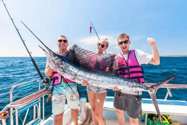 Three individuals proudly holding a sailfish on a boat, celebrating their successful catch during a thrilling deep-sea fishing adventure in Phuket.
