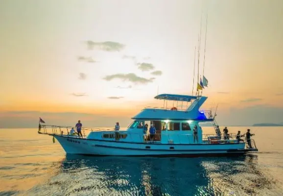A boat sails across the calm ocean, bathed in the warm, golden hues of a beautiful sunset over the Andaman Sea.