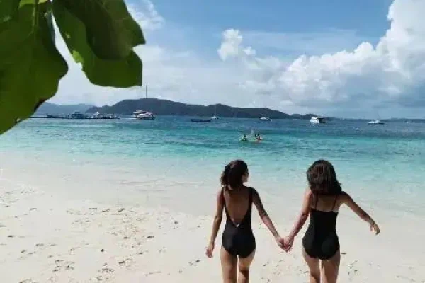 Two women in swimsuits stroll along the beach, enjoying the sun and the ocean breeze.